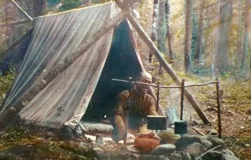 outdoors man in a canvas tent with bushcraft pots on fire